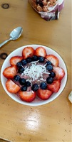 A bowl of strawberries, blueberries, coconut shavings, and yogurt.